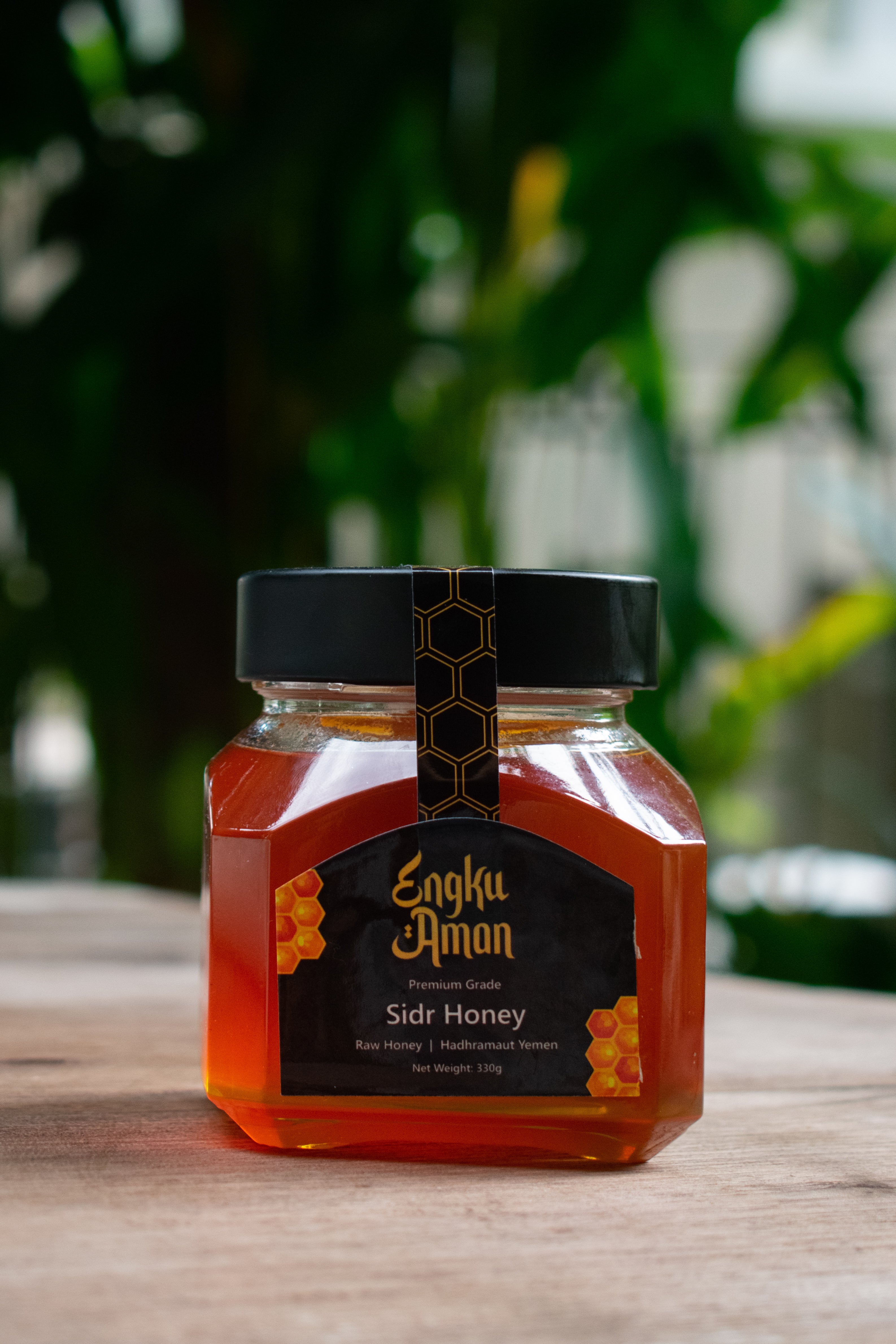 Jar of Sidr Honey with a black lid on a wooden surface, blurred greenery in the background